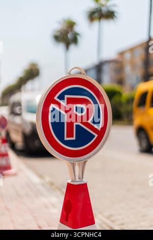 Un segnale di assenza di parcheggio è chiaramente visibile in una vivace giornata di sole. Le palme si innalzano sullo sfondo lungo una strada trafficata piena di parcheggiate e in movimento Foto Stock