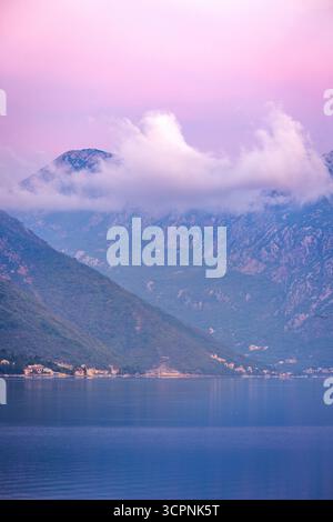 Calmo prima dell'alba sulla baia di Cattaro, in Montenegro, con montagne nebbiose, morbide nuvole e cielo blu-rosa che si riflette nelle acque tranquille prima dell'alba. Foto Stock