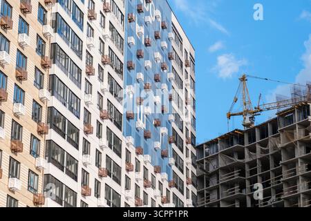 Un nuovo edificio residenziale presenta un'architettura moderna mentre un cantiere attivo è visibile sullo sfondo, su un cielo limpido. Foto Stock