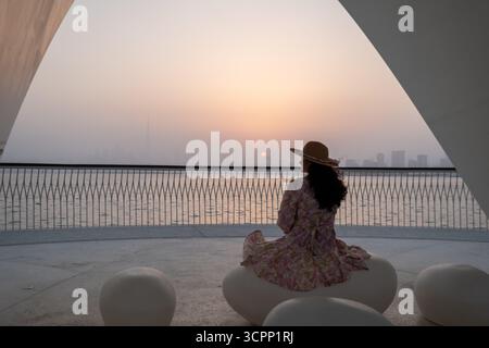 Donna seduta sotto una moderna tettoia al tramonto del porto di dubai creek, viaggi di lusso e stock di stile di vita in 4K pro res Foto Stock