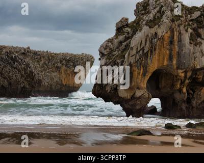Spiaggia nascosta e grotte marine frastagliate - spiaggia isolata tra imponenti scogliere calcaree con grotte marine e onde che si infrangono in una giornata drammatica e travolgente Foto Stock