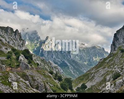 Picchi calcarei baciati dalle nuvole a Picos Europa - Vista maestosa e spettacolare di montagne calcaree frastagliate parzialmente oscurate da nuvole sospese basse e Foto Stock