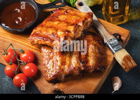 Costolette di ricambio piccanti e grigliate di un barbecue estivo servite con peperoncino caldo e pomodori freschi su un vecchio tagliere in legno vintage Foto Stock