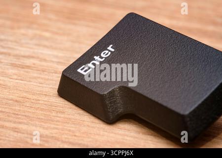 Fotografia macro del tasto Invio nero staccato dalla tastiera di un computer, posizionato su una superficie di legno. Ideale per l'uso editoriale, blog tecnologici. Foto Stock