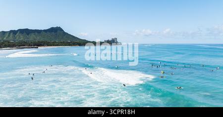 Vista aerea delle onde turchesi che si infrangono lungo la costa, i surfisti che punteggiano l'oceano sullo sfondo di Diamond Head, Waikiki, Honolulu, Hawaii, Stati Uniti. Foto Stock