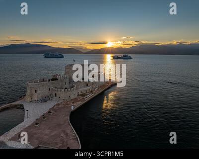 Vista aerea del castello di Bourtzi in piedi di guardia nelle acque tranquille, bagnato dal caldo bagliore del sole che tramonta, Nauplia, Argolide, Grecia. Foto Stock