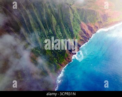 Vista aerea delle scogliere spettacolari che incontrano l'oceano turchese sotto un velo di nebbia, una sinfonia di colori e texture lungo la costa, Napali, Hawaii, Stati Uniti. Foto Stock