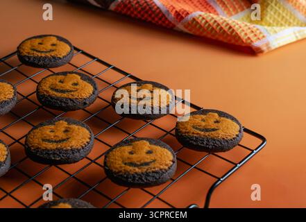 Biscotti di zucca al cioccolato fatti in casa poggiati su una griglia di raffreddamento su sfondo arancione. un asciugamano da cucina dai colori autunnali sul lato Foto Stock