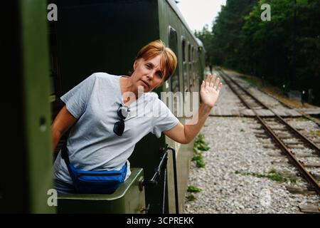 Donna di mezza età che salta dal treno d'epoca alla stazione ferroviaria di Mokra Gora. Sargan Eight - una popolare destinazione turistica in Serbia. Foto Stock