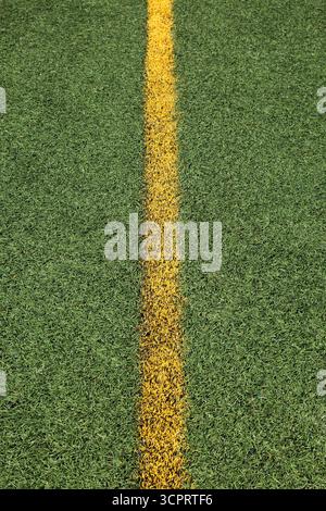 Vista dall'alto della linea dritta verniciata a spruzzo giallo sull'erba artificiale verde su campi sportivi a uso multiplo. Foto Stock