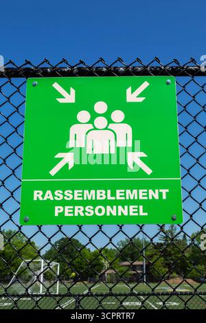 Frecce bianche che puntano a un gruppo di 4 persone in forma di contorno che indicano l'area di raccolta sul simbolo verde fluorescente fissato alla recinzione a rete metallica. Foto Stock
