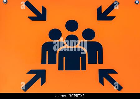 Frecce nere che puntano a un gruppo di 4 persone con un contorno sagomato che indica un'area di raccolta su un simbolo arancione. Foto Stock