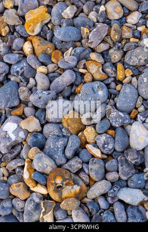 Pietre colorate sparse lungo la riva, che mostrano una varietà di texture e sfumature in un ambiente naturale costiero Foto Stock