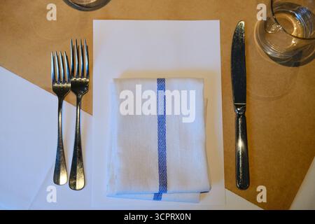 Elegante tavolo con coltello e forchette, carta bianca come mockup e tovagliolo a strisce piegato Foto Stock