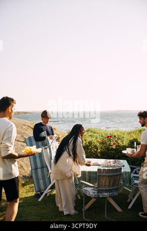 Gli amici multirazziali preparano un tavolo per una cena nel cortile posteriore nella giornata di sole Foto Stock
