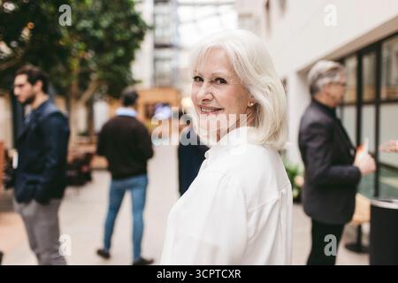 Ritratto di un'esperta di affari donna sorridente con capelli bianchi che si guardano sulla spalla Foto Stock