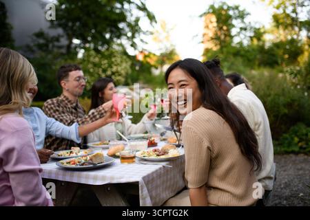 Ritratto di una giovane donna felice che si diverte a cenare a un incontro sociale con gli amici nel cortile posteriore Foto Stock