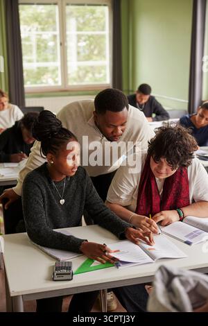 Vista ad angolo alto dell'insegnante di sesso maschile che aiuta gli studenti a risolvere l'equazione matematica nelle classi medie Foto Stock