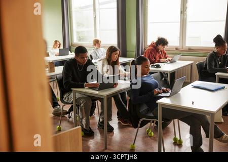 Studenti adolescenti di sesso maschile e femminile che studiano con un computer portatile in classe a scuola Foto Stock
