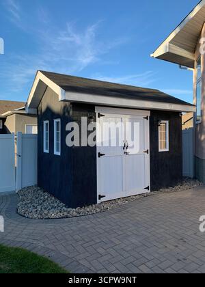 Moderno giardino con doppie porte e finestre bianche, circondato da giardini di ghiaia su un patio soleggiato vicino all'esterno di casa. Foto Stock