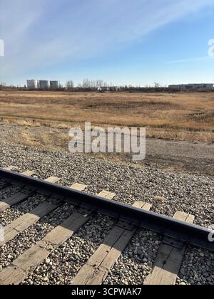 I binari ferroviari tagliano attraverso una prateria dorata con silos in lontananza. Foto Stock