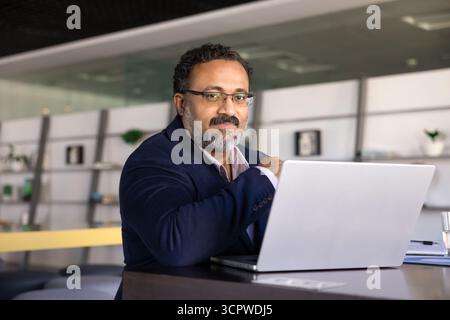 Ritratto di un uomo d'affari indiano seduto alla scrivania con un computer portatile Foto Stock