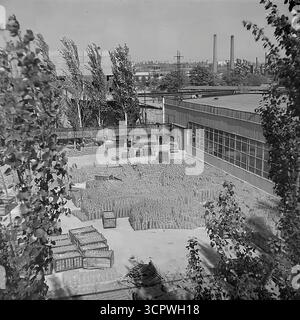 Il deposito all'aperto dello Slavyansk Fittings and Insulator Plant (AIZ) è pieno di migliaia di isolanti in ceramica finiti nella RSS Ucraina negli anni '1970 Questa foto d'archivio monocromatica cattura l'immensa scala della produzione di massa dell'era sovietica, con prodotti impilati ordinatamente in casse e su pallet. Una grande gru a cavalletto attraversa il cantiere, utilizzata per la logistica e la spedizione di questi componenti essenziali per i progetti di elettrificazione dell'URSS, mostrando la potenza industriale della regione del Donbas. Foto Stock