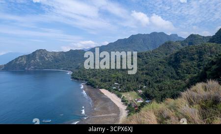 Vista aerea di un villaggio costiero con case semplici, spiaggia sabbiosa e lussureggianti palme tropicali, catturando la bellezza e la tranquillità della vita dell'isola. Foto Stock