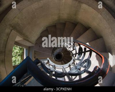 Scala architettonica a spirale Vista in basso - suggestiva vista dall'alto di una storica scala a chiocciola in pietra con ringhiera in ferro battuto scuro, che enfatizza Foto Stock