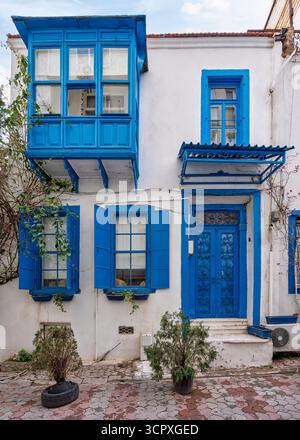Finestre blu vibranti, persiane e finestre a bovindo ornate su una tradizionale casa bianca a Smirne, Turchia. Architettura classica dell'Egeo con fogliame verde Foto Stock