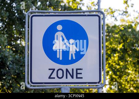 Un segno quadrato indica una zona designata. Il cartello mostra una madre e un bambino che si tengono per mano all'interno di un cerchio blu sopra la parola ZONE Foto Stock