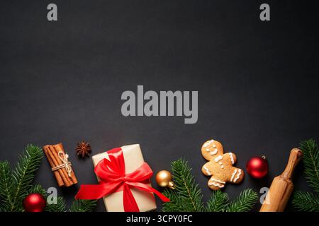 Sfondo piatto natalizio. Biscotti al pan di zenzero, scatola regalo, spezie e decorazioni natalizie sul nero. Foto Stock