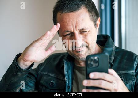 Uomo con giacca in pelle che saluta durante una videochiamata sull'app per smartphone, moderna comunicazione online e concetto di connessione virtuale. Messa a fuoco selettiva. Foto Stock