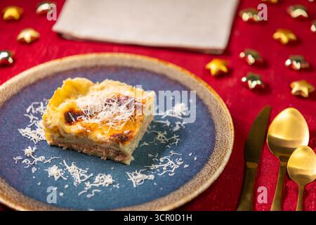 Lasagne italiane al forno con formaggio grattugiato su un piatto blu, pronte per essere servite tra le decorazioni natalizie Foto Stock