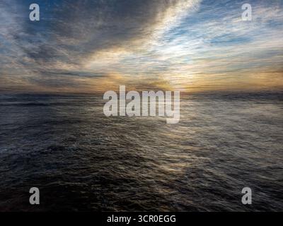Uno splendido tramonto a Huelva, in Spagna, mostra vivaci sfumature di arancione e blu sul cielo e sull'oceano, meravigliosamente catturati durante una lunga esposizione. Foto Stock