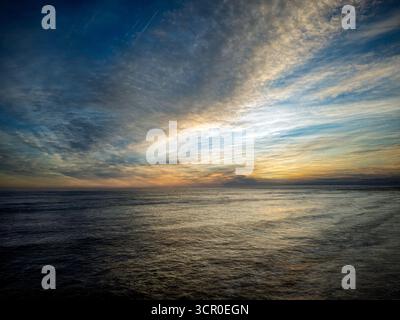 Uno splendido tramonto a Huelva, in Spagna, mostra vivaci sfumature di arancione e blu sul cielo e sull'oceano, meravigliosamente catturati durante una lunga esposizione. Foto Stock