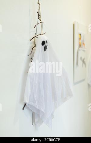 Una decorazione fantasma spettrale realizzata con tessuto bianco e ramoscelli è appesa a una parete, aggiungendo un tocco di festa all'atmosfera di Halloween nella camera. Foto Stock