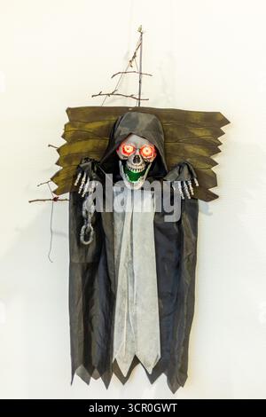 Una spaventosa figura scheletrica con occhi rossi brillanti e un grin minaccioso appeso a un muro, aggiungendo un tocco inquietante alle feste di Halloween. E' un perfec Foto Stock