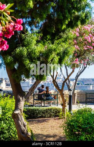 Coppia seduta su una panchina, mentre si gode la vista dei giardini Lower Barrakka a la Valletta, Malta Foto Stock