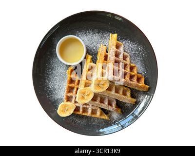 Gustosi waffle con banana e panna su piatto scuro isolato su sfondo bianco. Vista dall'alto. Foto Stock