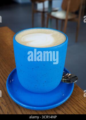 Latte caldo con schiuma Art servito in tazza blu minimalista su tavolo in legno Foto Stock
