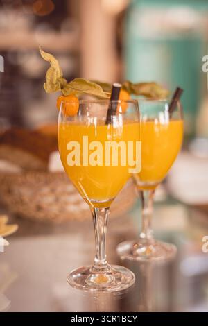 Due vivaci cocktail all'arancia, guarniti con frutta e foglie, riposano su una superficie riflettente mentre i clienti si godono un pomeriggio di sole in un vivace caffè, CEL Foto Stock