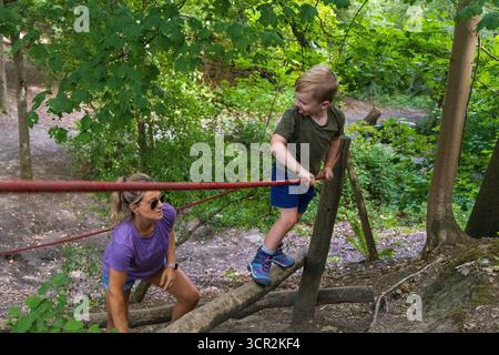 I bambini giocano su scivoli e arrampicate in un parco giochi naturale circondato da alberi. Foto Stock