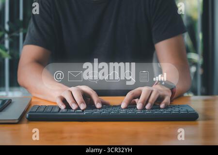 Uomo d'affari che utilizza la tastiera del computer per e-mail, messaggistica istantanea, sistema cloud, dati di ricerca, note documenti e icone grafiche aziendali. Foto Stock