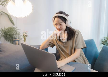 Una giovane donna che indossa le cuffie interagisce con il suo notebook in diversi stati d'animo, dall'emozione alla concentrazione, mostrando momenti di gioco di stile di vita moderno, l Foto Stock