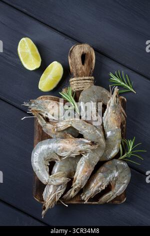 Gamberetti freschi, crudi, gamberetti di tigre vannamei, su un tagliere di legno, con fette di lime e condimenti Foto Stock