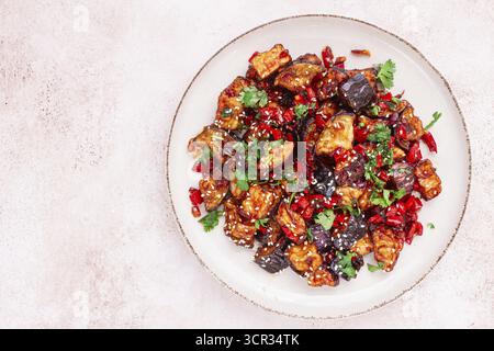 Melanzane fritte, stile cinese, in salsa dolce e acida, con pepe e semi di sesamo. su un piatto bianco Foto Stock