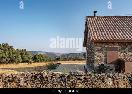 Costruzione rustica in pietra naturale con tetto in ardesia, circondata da un muro di pietra a secco e da un giardino selvaggio autoctono Foto Stock