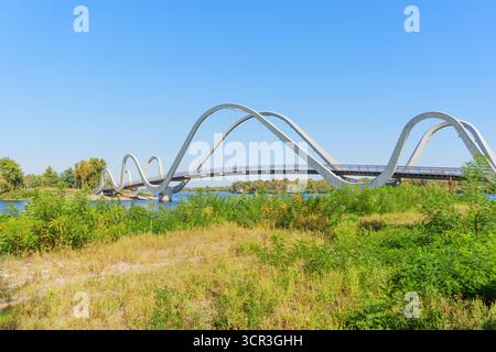 Lo splendido ponte ondulato si estende su un sereno corpo d'acqua, incorniciato da una vibrante vegetazione a Kiev. Foto Stock