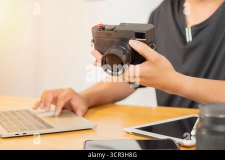 Giovane fotografo maschio che controlla gli scatti e modifica le foto sul suo computer mentre lavora dall'ufficio. Messa a fuoco selettiva. Foto Stock